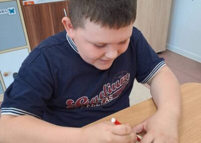 Chłopiec rysuje na małym okrągłym papierze przy stole w pokoju z półkami z grami.