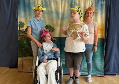 Cztery osoby z kolorowymi nakryciami głowy na tle krajobrazu i tablicy do koszykówki w sali gimnastycznej.