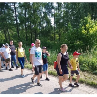 Grupa osób różnych wieku idzie chodnikiem w otoczeniu zielonego lasu.