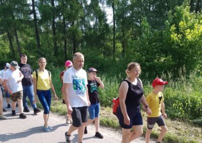 Grupa osób różnych wieku idzie chodnikiem w otoczeniu zielonego lasu.