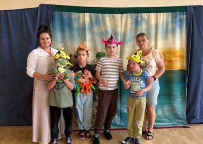 Dzieci w kolorowych czapkach z pluszakami stoją z dwiema kobietami na sali gimnastycznej.