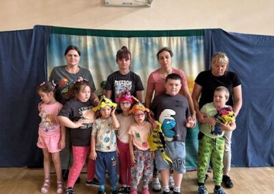 Dzieci z maskotkami i czapkami stoją z dorosłymi pod koszem w sali gimnastycznej.