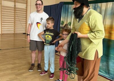 Dwóch dorosłych i dwoje dzieci stojących w sali gimnastycznej z siatką rybacką i ścianką wspinaczkową.