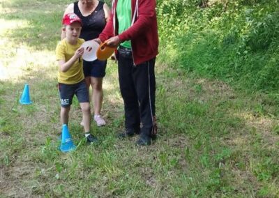 Trójka osób na trawie z dyskami sportowymi i pachołkami treningowymi w lesie.