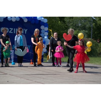 Dzieci i dorośli na drewnianej platformie z balonami i dekoracją z niebiesko-białych balonów.