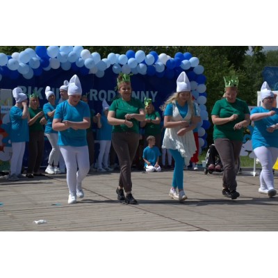 Osoby tańczące na drewnianej scenie z dekoracjami z niebieskich i białych balonów.