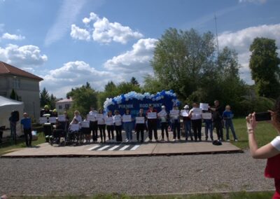 Grupa osób na drewnianej platformie z tabliczkami podczas rodzinnego pikniku na świeżym powietrzu.