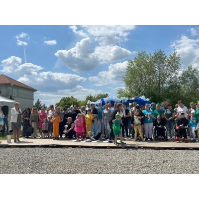 Grupa ludzi, w tym dzieci i osoby na wózkach, stoi na zewnątrz przy dekoracji balonowej.