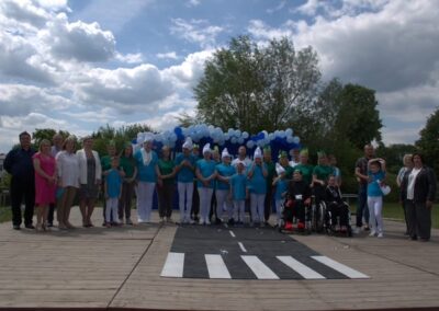 Grupa osób na drewnianej scenie z dekoracją balonową i makietą przejścia dla pieszych.