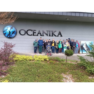 Grupa osób stoi przed budynkiem Oceanika z napisem i oceanicznym symbolem na elewacji.