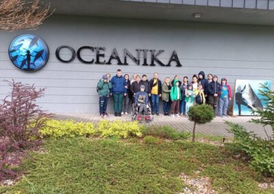 Grupa osób stoi przed budynkiem Oceanika z napisem i oceanicznym symbolem na elewacji.