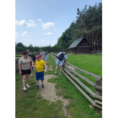Ludzie spacerują obok drewnianego ogrodzenia przy wiejskiej chacie i lesie.