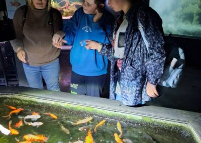Trzy osoby obserwują kolorowe ryby w akwarium wewnątrz pomieszczenia.