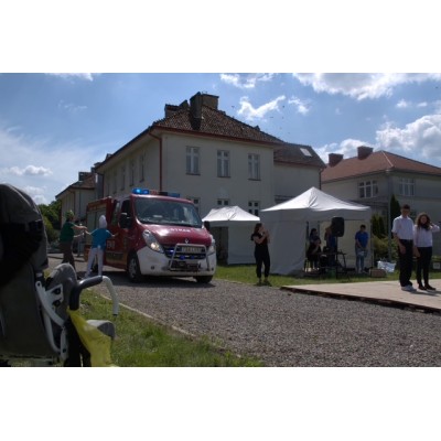 Czerwony wóz strażacki na żwirowej drodze obok namiotów i ludzi przy budynkach mieszkalnych.