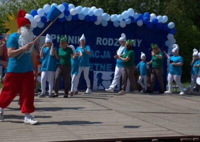 Grupa osób w kostiumach smerfów i innych postaci na scenie dekorowanej balonami.