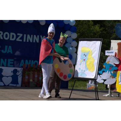 Dwie osoby przebrane za Smerfy podczas plenerowego występu z paletą i rysunkiem Smerfetki.