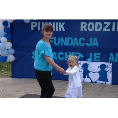 Kobieta i dziewczynka trzymające się za ręce na drewnianej scenie z niebiesko-białą dekoracją balonową.