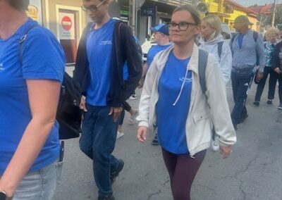 Kilka osób w niebieskich koszulkach maszeruje razem, uśmiechając się do aparatu podczas wydarzenia na świeżym powietrzu.