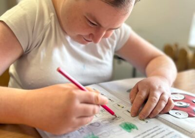 Zbliżenie na rękę trzymającą czerwony ołówek nad kartą z biedronką oraz kółkami z literami przygotowanymi do przyklejenia.