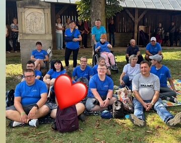 Kilka osób w niebieskich koszulkach maszeruje razem, uśmiechając się do aparatu podczas wydarzenia na świeżym powietrzu.