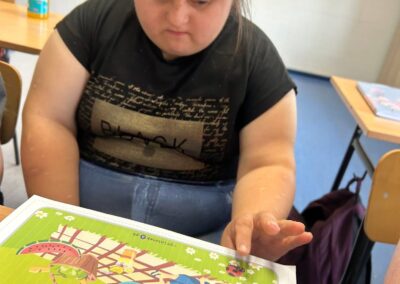 Uczestnik siedzi przy stole i ogląda dużą kolorową stronę z ćwiczeniami oraz obrazkami.