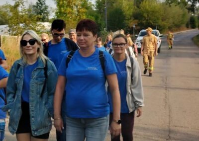 Duża grupa uczestników maszeruje drogą, a w tle widać pojazd służb i osobę w mundurze zabezpieczającą trasę.