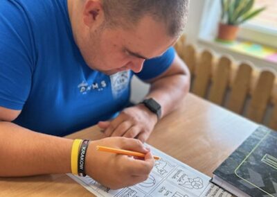 Uczestnik wypełnia ołówkiem kartę pracy leżącą na stole i skupia się na poleceniach.