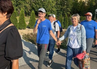 Uczestnicy idą w grupie; na pierwszym planie para trzyma się za ręce, a obok inni maszerują i machają.