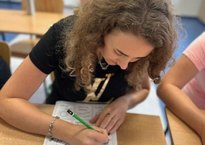 Uczestniczka zapisuje odpowiedzi na wydrukowanej karcie ćwiczeń a obok leżą przybory szkolne.