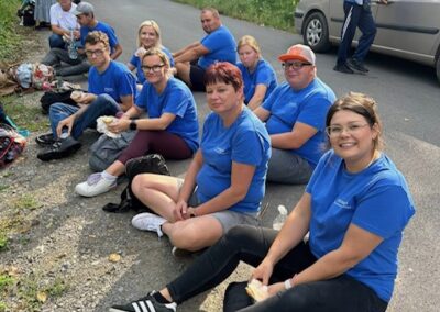 Uczestnicy siedzą na poboczu podczas postoju i jedzą przekąski; obok stoją samochody i pozostali uczestnicy.