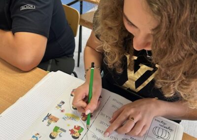 Na stole leży otwarta książka ćwiczeń oraz karta pracy z narysowanymi liniami i zaznaczeniami przy zadaniach.