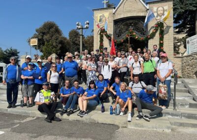 Duża grupa uczestników pozuje do wspólnego zdjęcia przed bramą prowadzącą na teren kościoła lub kaplicy.