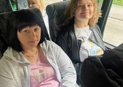 Cztery osoby siedzące w autobusie, za oknem zieleń i chodnik.