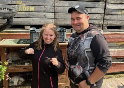 Dwoje ludzi stoi obok klatek z królikami na tle drewnianych skrzyń na zewnątrz.