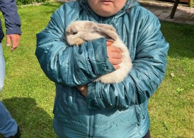 Dziewczynka w niebieskiej kurtce trzymająca białego królika na trawie w ogrodzie.