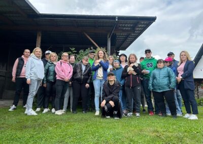 Grupa osób w sportowych ubraniach stoi na trawie przed drewnianą zabudową pod zachmurzonym niebem.