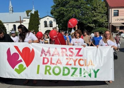Marsz dla życia i rodziny z czerwonymi balonami, uczestnicy niosą banner, kościół w tle.