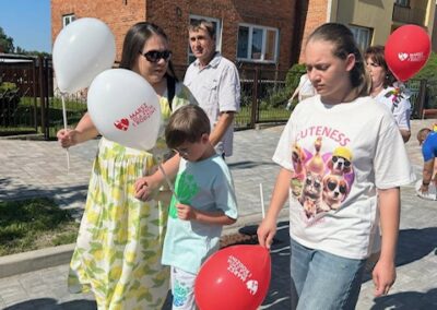 Ludzie spacerują chodnikiem z balonami z napisem Marsz Godności w słoneczny dzień.