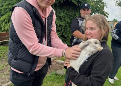 Młoda kobieta trzyma królika, a mężczyzna głaszcze go na zewnątrz na trawie.