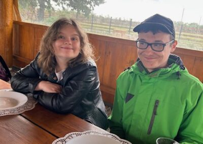 Dwoje młodych ludzi siedzących przy drewnianym stole na zewnątrz z pustymi talerzami i napojem.