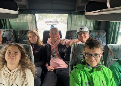 Pięć młodych osób siedzi w autobusie na fotelach z zielonymi zasłonami i informacją bezpieczeństwa.