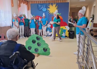 Osoby przebrane za Smerfy wykonują przedstawienie dla starszej osoby na wózku inwalidzkim.