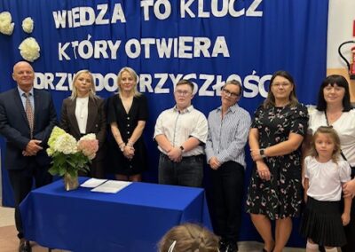 Uczestnicy ustawieni w rzędzie pozują do zdjęcia przed scenografią z hasłem Wiedza to klucz, po prawej stoi mała dziewczynka.