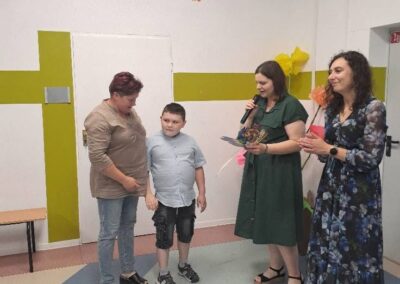 Dziecko podczas odbierania dyplomu od nauczyciela w sali przedszkolnej.