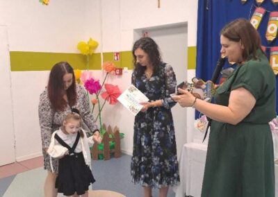 Dziecko z kwiatami pozuje do zdjęcia z nauczycielami po wręczeniu dyplomu.