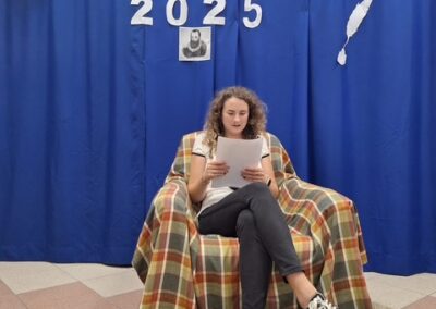 Kobieta siedzi na fotelu i czyta książkę przed granatową kurtyną Narodowe Czytanie 2025.