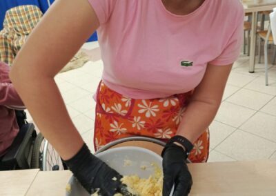 Osoba w rękawiczkach miesza i rozciera składniki w misce ustawionej na stole