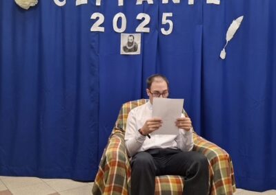 Uczestnik siedzi na fotelu i czyta książkę, za nim widoczny napis Narodowe Czytanie 2025.