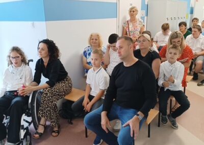 Szeroki widok korytarza szkolnego wypełnionego uczestnikami uroczystości.