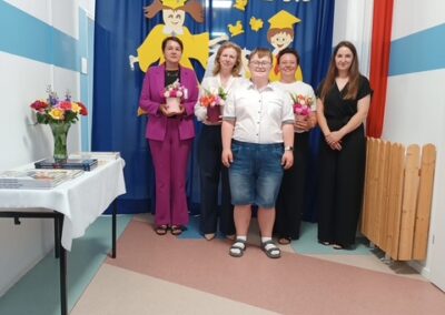 Uczeń pozuje do pamiątkowego zdjęcia z nauczycielkami trzymającymi kwiaty.